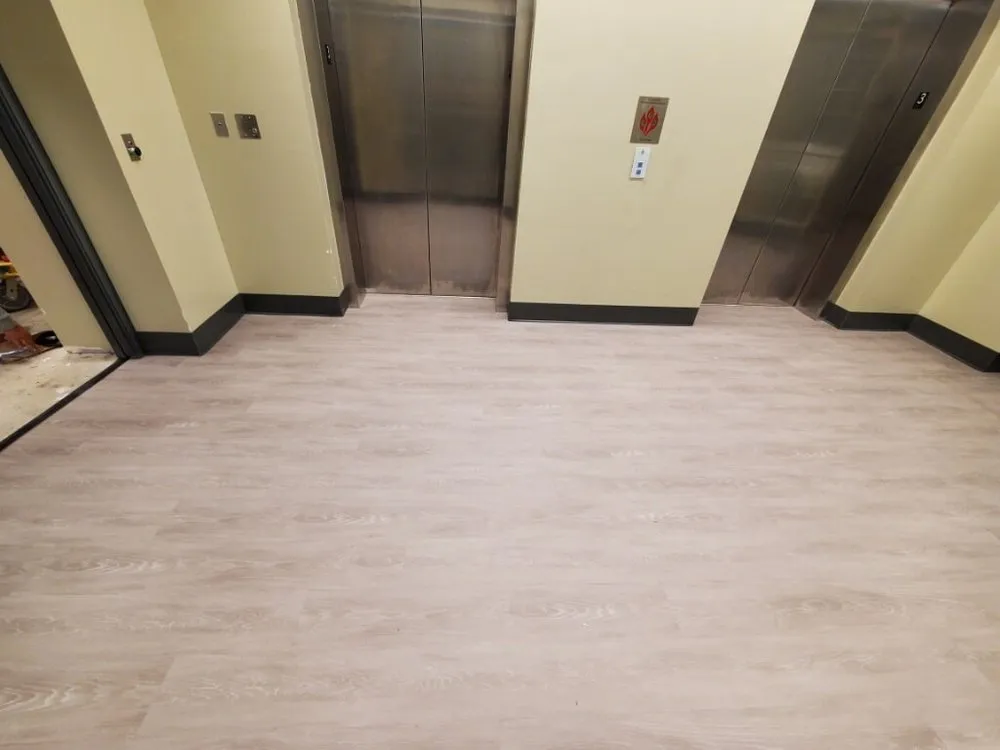 Pale wood-look plank floor in an elevator lobby with beige walls.